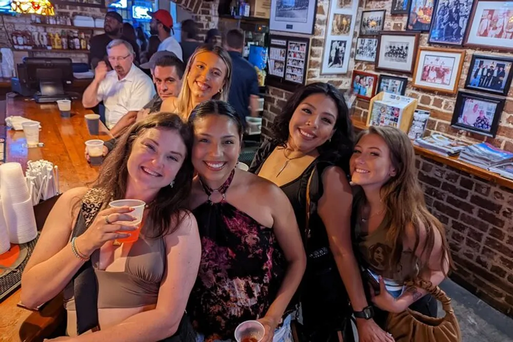A group of smiling people enjoying themselves at a bar with a brick wall and framed photographs in the background