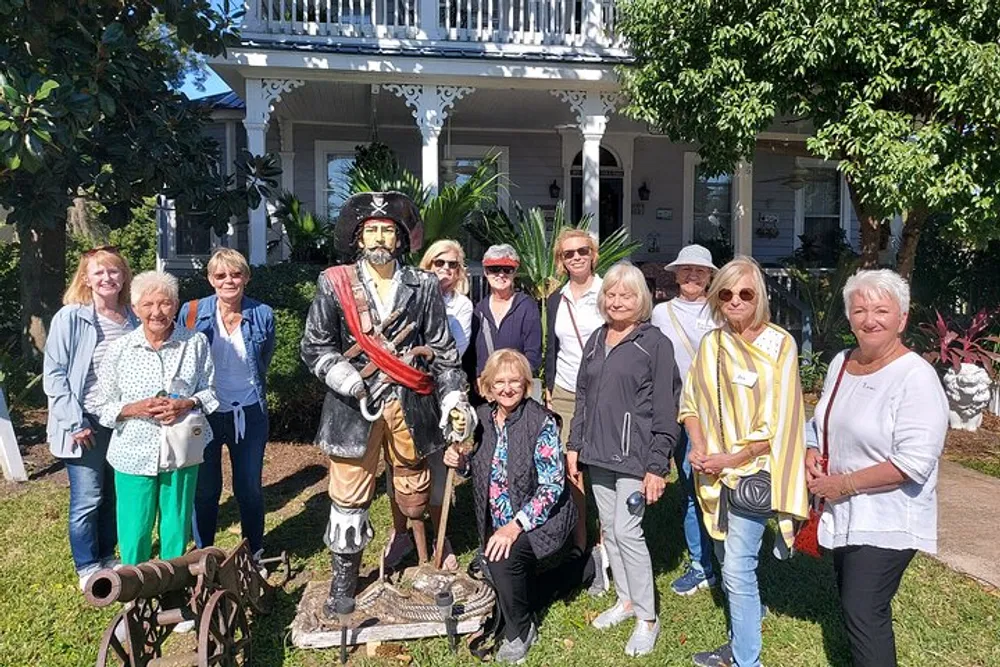 A group of people is posing for a photo with a pirate statue in front of a house with a classic balcony