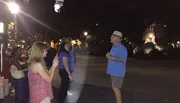 A group of people are listening to a man who appears to be giving an outdoor evening tour.