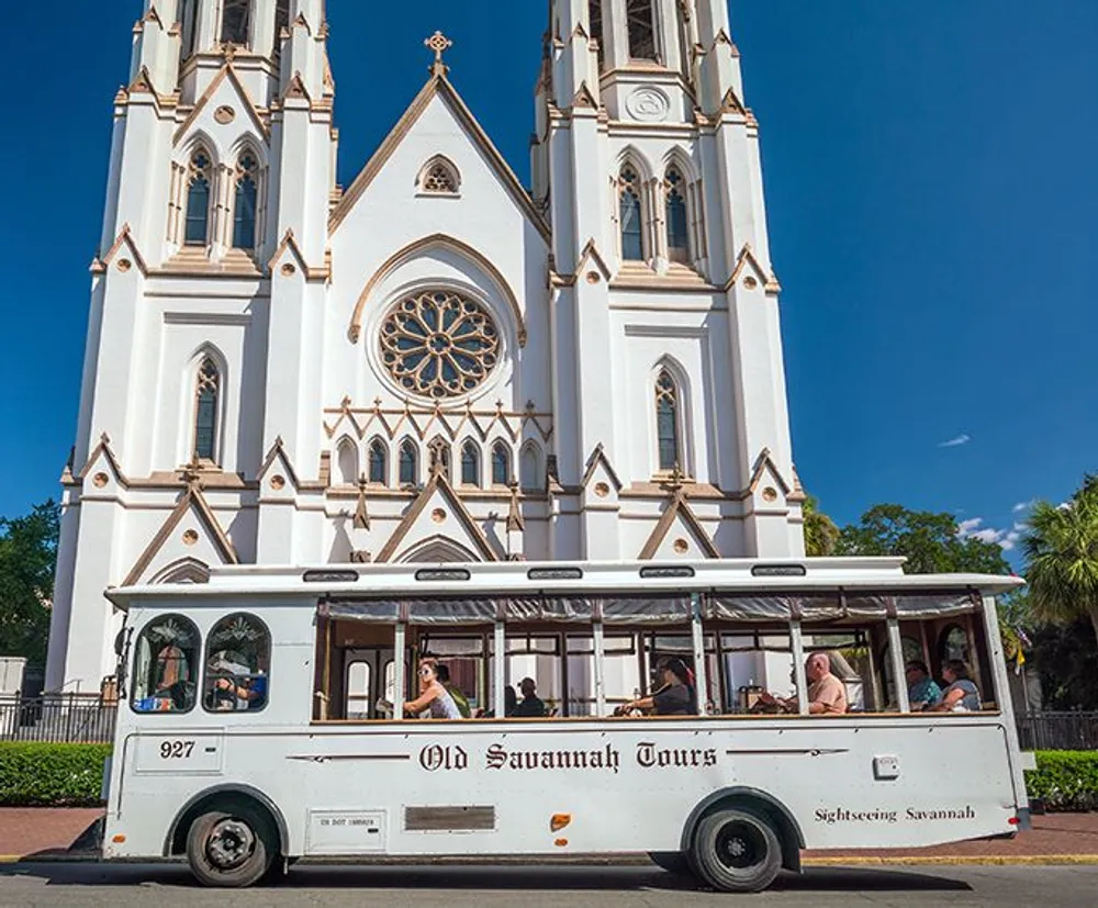 A sightseeing tour bus labeled Old Savannah Tours is passing by a large gothic-style cathedral with twin spires on a sunny day