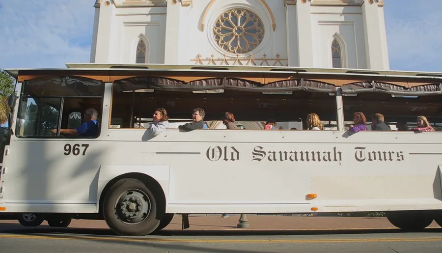 A group of people are riding on a tourist trolley labeled Old Savannah Tours in front of a historic building.