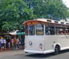 A group of people are riding a white trolley labeled Old Savannah Tours near a historic building with a sign for the Pirates House