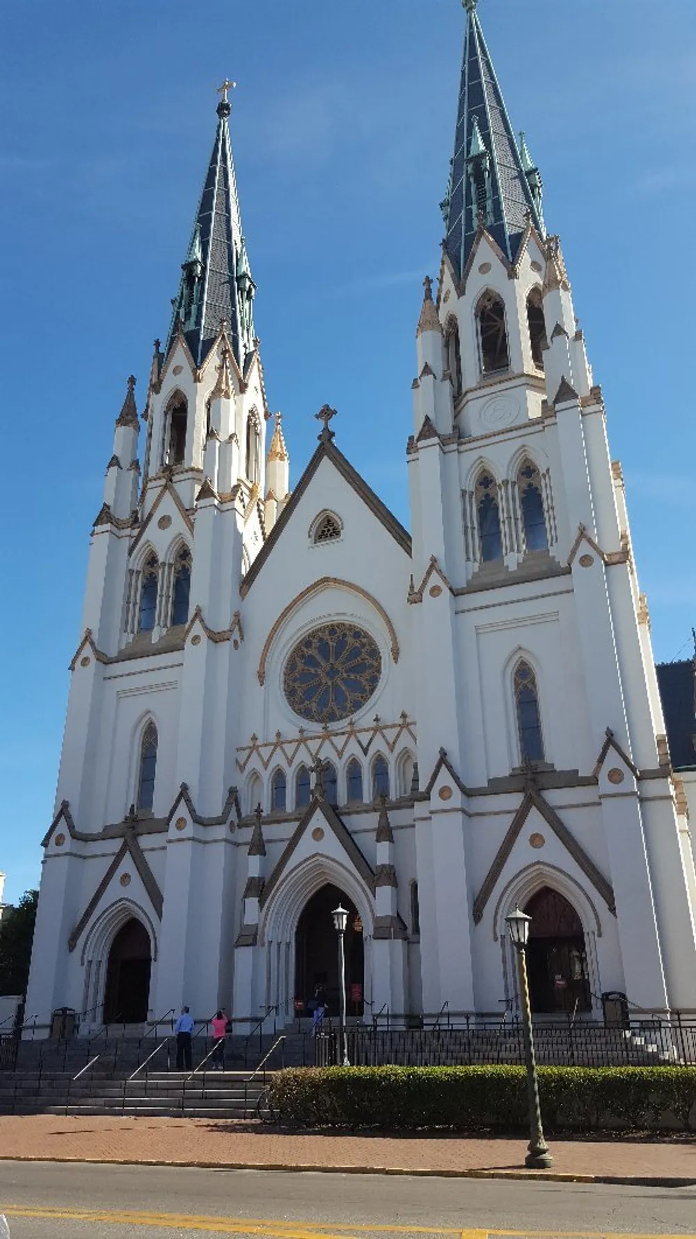 This image shows a grand white cathedral with two towering spires against a clear blue sky with people approaching its entrance