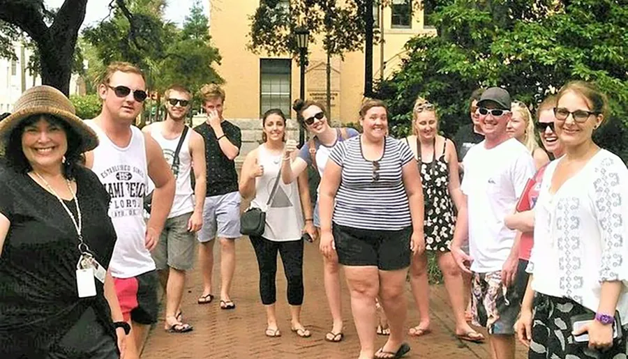 A group of smiling people, including a tour guide wearing a hat and badge, is posing for a group photo outdoors on a sunny day.