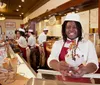 Four smiling employees in matching uniforms pose in front of Leopolds Ice Cream shop which boasts a vintage aesthetic with its cursive neon sign