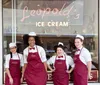 Four smiling employees in matching uniforms pose in front of Leopolds Ice Cream shop which boasts a vintage aesthetic with its cursive neon sign