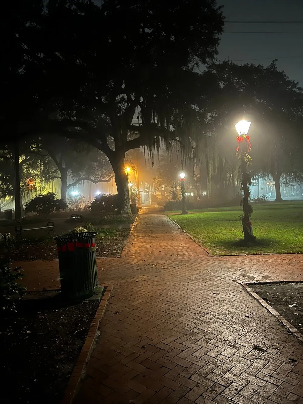 A foggy evening view of a park path lined with old-fashioned lampposts adorned with red bows evoking a quiet serene ambiance