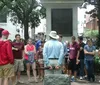 A group of people appear to be on an outdoor guided tour listening to a person who is likely the tour guide standing in front of them with his back to the camera