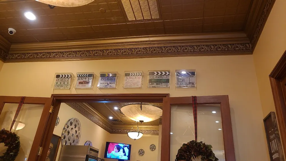 The image shows an interior with decorative clapperboards displayed on a wall above a large mirror with a vintage style ceiling and a television screen visible in the reflection