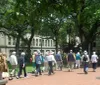 A group of people possibly on a guided tour are gathered in a park with lush green trees
