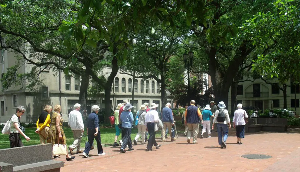 A group of people likely on a tour walk through a green tree-shaded park area in an urban setting