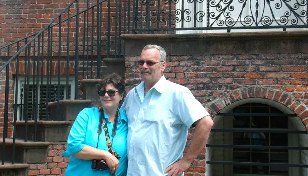 A man and a woman are standing in front of a brick building with a metal stair railing on the side