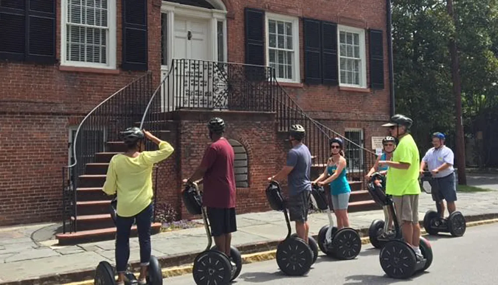 A group of people wearing helmets are standing on Segways on a street possibly on a guided tour