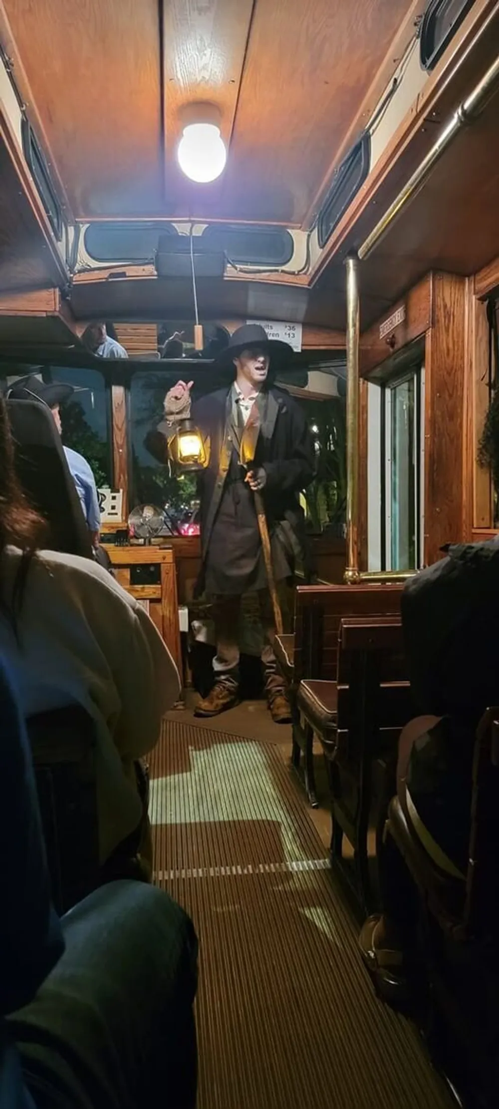 A person in a period costume holding a lantern stands inside a vintage train carriage seemingly addressing the passengers