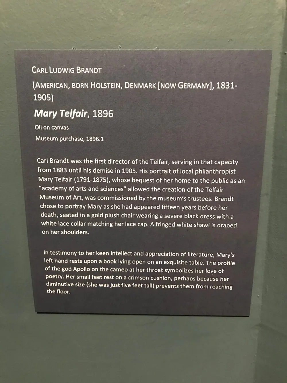 The image shows a plaque describing the artwork Mary Telfair painted in 1896 by Carl Ludwig Brandt detailing its background the artists tenure as the first director of the Telfair museum and the elements of the portrait that reflect Mary Telfairs character and interests