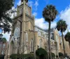 The image features a grand ornate church with Gothic architectural elements framed by palm trees against a partly cloudy sky