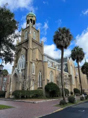 The image features a grand, ornate church with Gothic architectural elements, framed by palm trees against a partly cloudy sky.