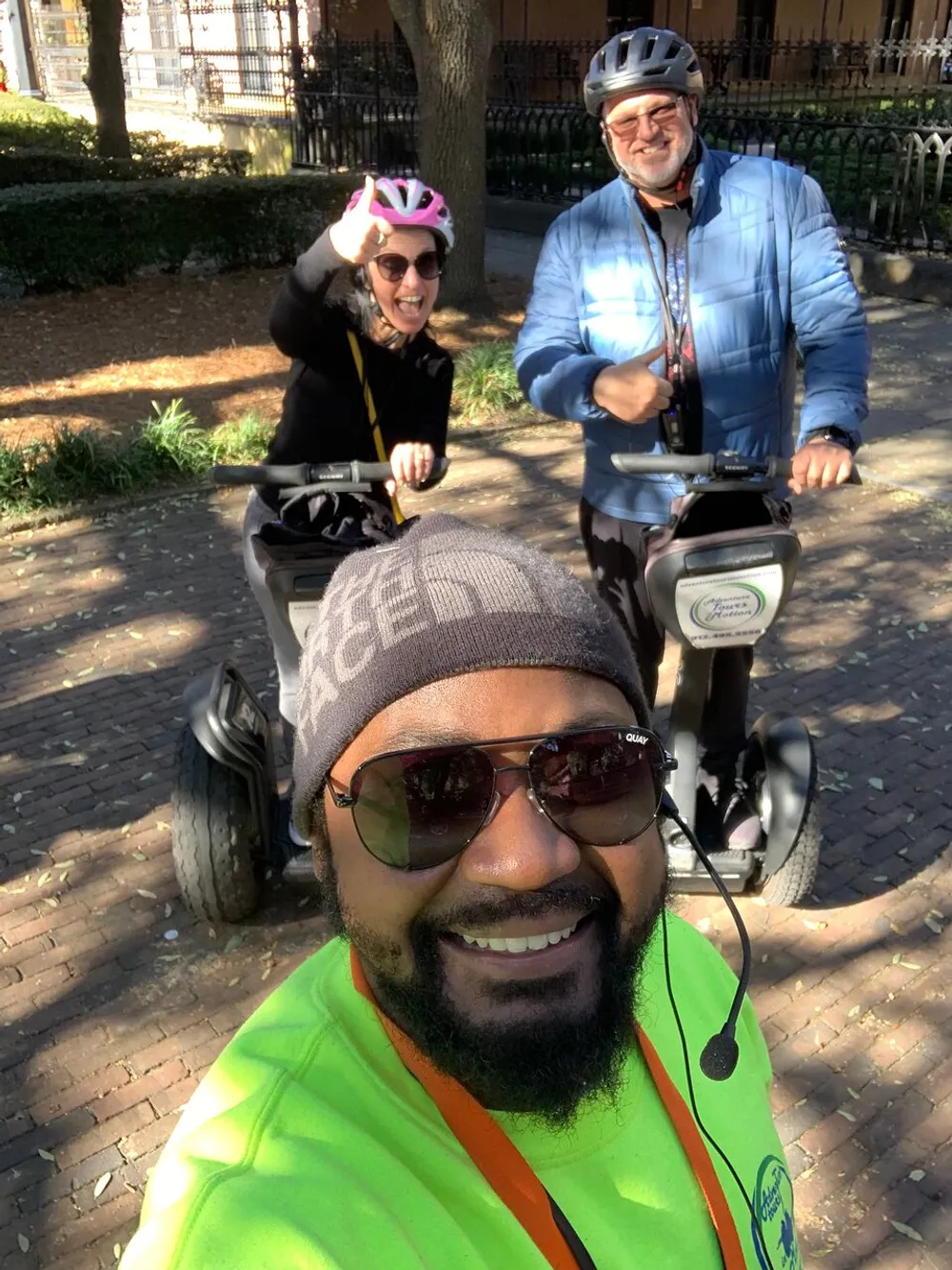 Three people are posing for a selfie with two of them on segways all wearing helmets and smiling in an outdoor setting