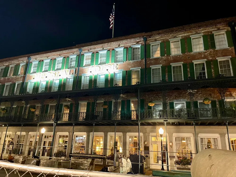 The image shows a well-lit multi-storied building with a traditional balcony facade at night evocative of New Orleans French Quarter architecture