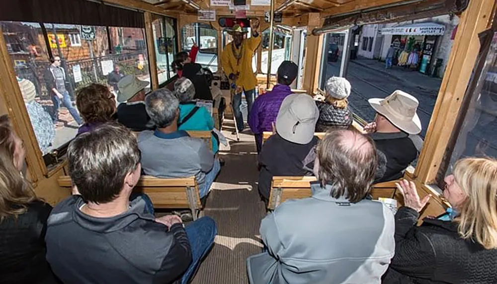 Passengers inside a trolley or tour vehicle are listening to a guide who is standing and speaking at the front