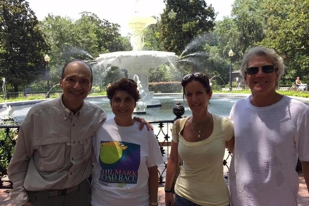 Three smiling adults are posing for a photo in front of a large ornate fountain on a sunny day