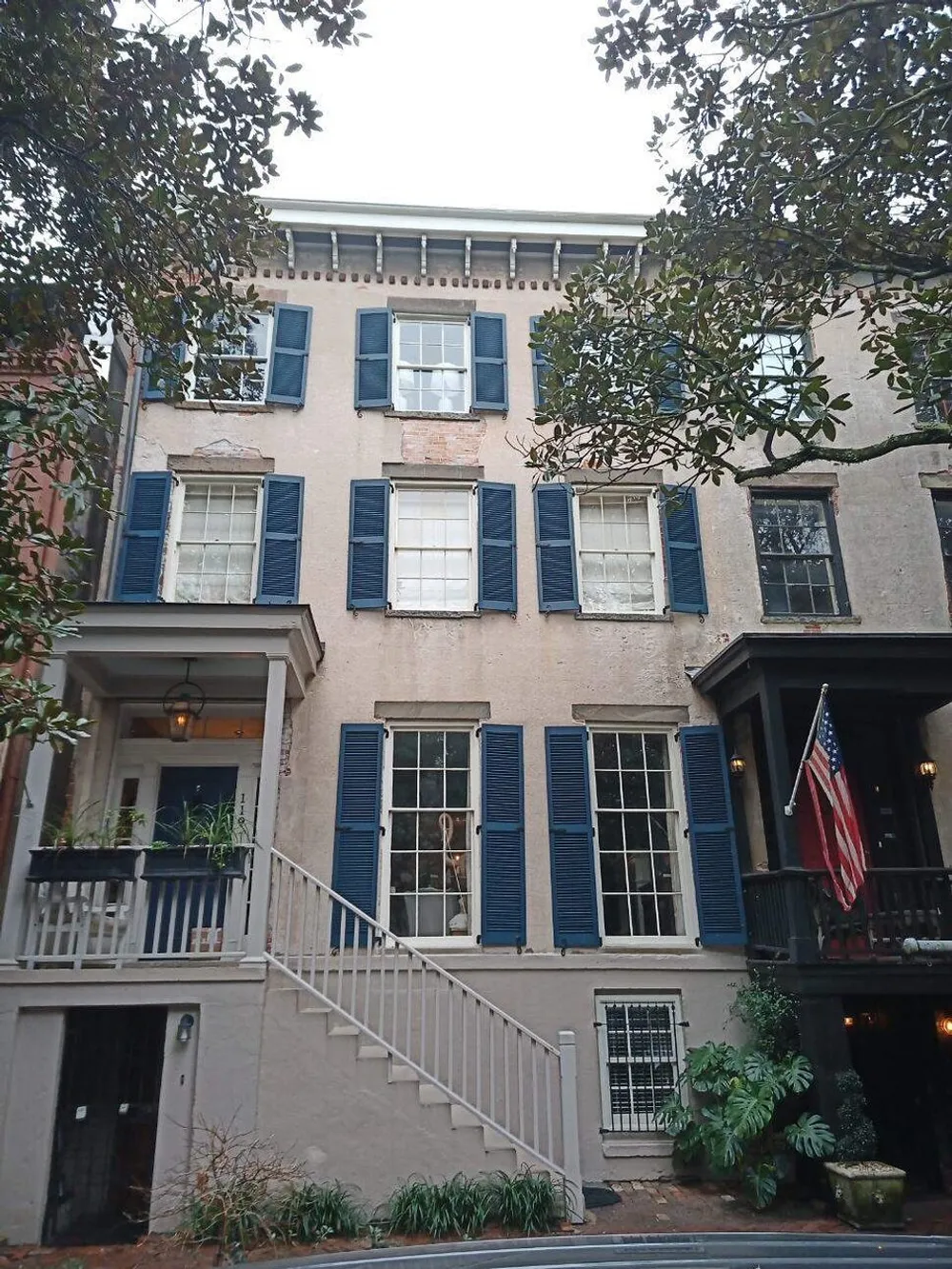 The image shows the facade of a charming three-story building with blue shutters an external staircase and a balcony adorned with an American flag