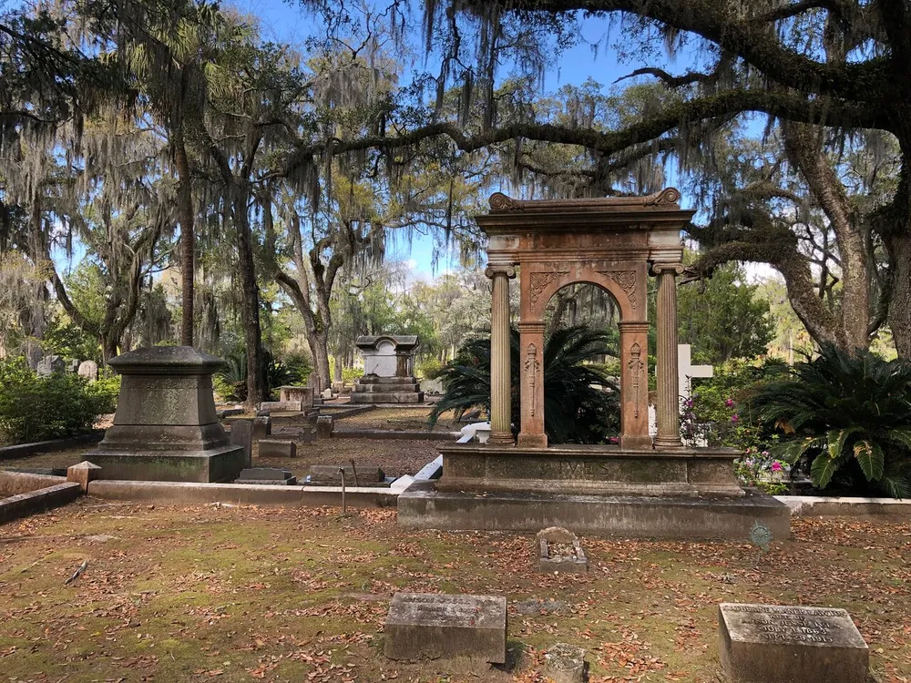 The image shows a serene and historic cemetery with moss-draped oak trees weathered gravestones and elaborate monuments
