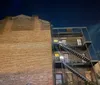 The image depicts an exterior brick wall of a multi-story building at night featuring a metal fire escape against a dark sky