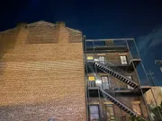 The image depicts an exterior brick wall of a multi-story building at night, featuring a metal fire escape against a dark sky.