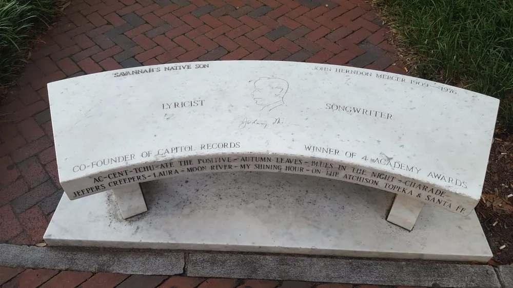 The image displays a curved bench with an engraved tribute to Savannahs Native Son John Herndon Mercer highlighting his achievements as a lyricist songwriter co-founder of Capitol Records and winner of Academy Awards