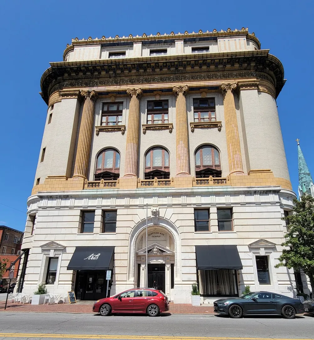 This image showcases a grand corner building with neoclassical architectural elements and street-level commercial space complemented by a clear blue sky and flanked by parked cars