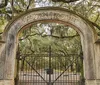 A person gives a presentation or tour in a cemetery pointing at a large rugged gravestone with detailed engravings and metal adornments