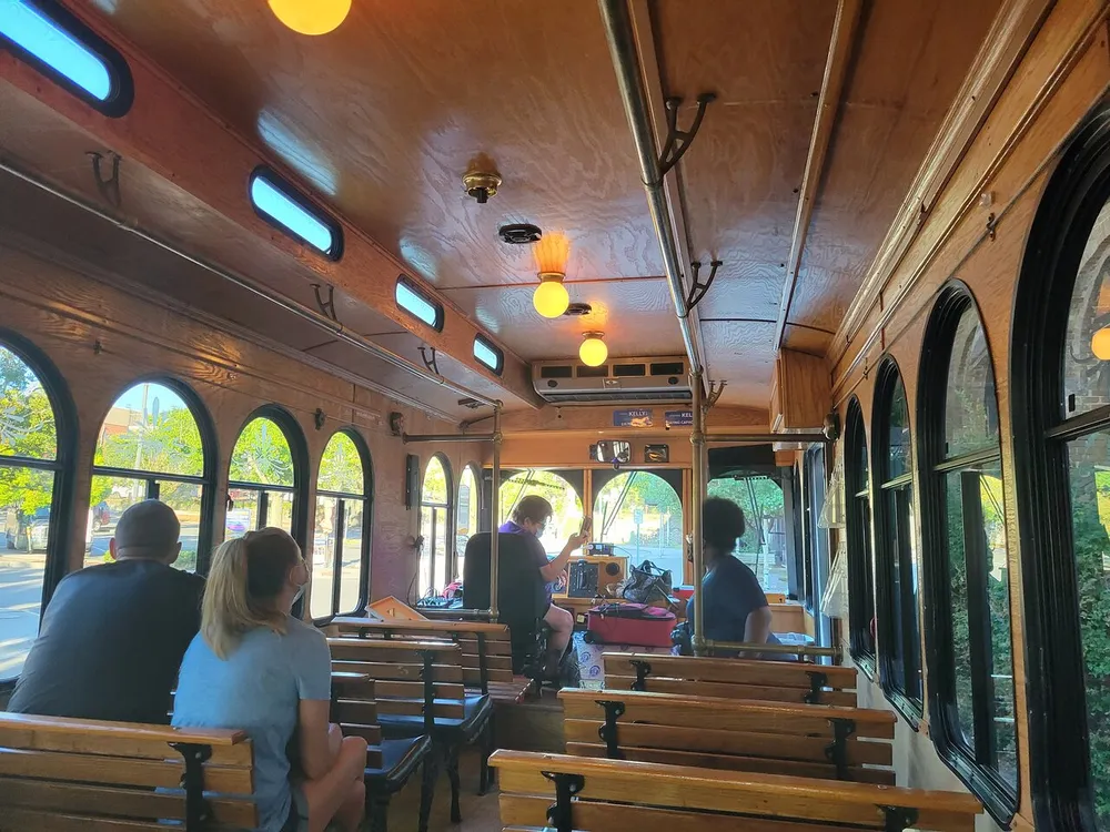 Passengers are seated inside a vintage-style trolley with wooden benches and arched windows bathed in warm light