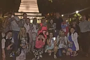 A group of people are posing for a photo at night, holding up books and making playful gestures near a monument.
