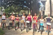 A group of people are smiling and posing with their bicycles on a sunny day, possibly during a group ride or a social event.