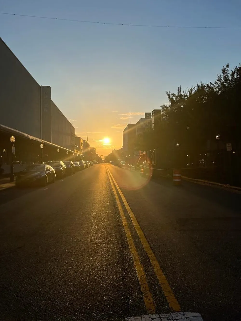 The image shows a serene sunset view down an urban street lined with parked cars and buildings with the sun casting a golden glow and long shadows on the pavement