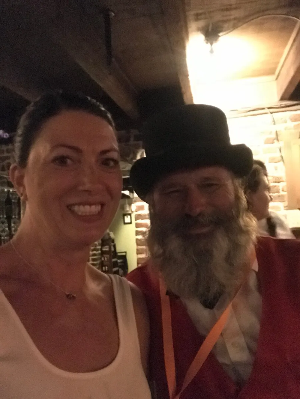 A woman and a man with a beard and top hat are taking a friendly selfie together