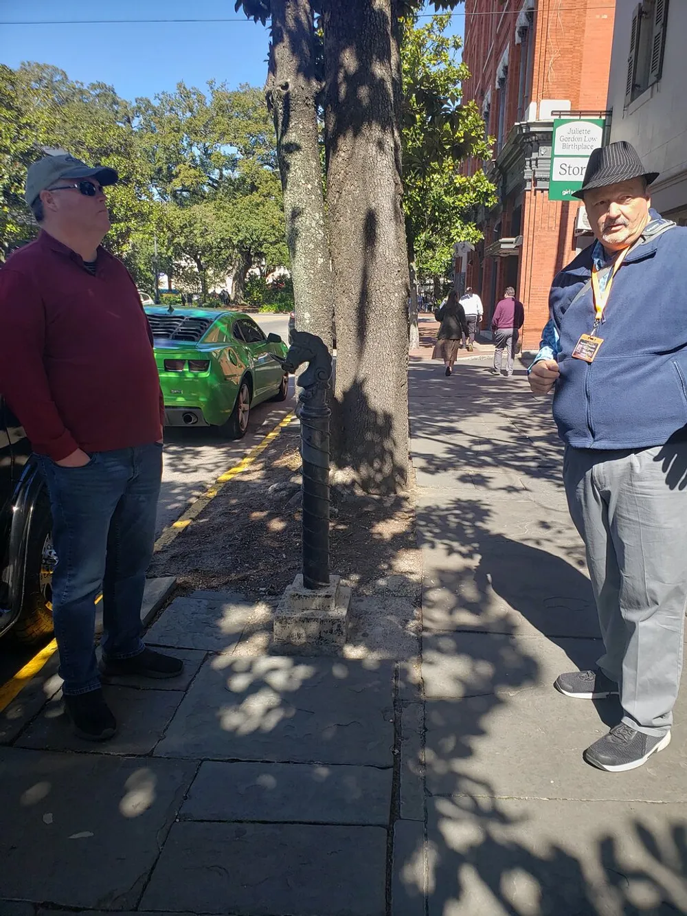 Two men are standing on a sidewalk having a conversation with a green car parked in the background and the sign Juliette Gordon Low Birthplace visible suggesting the location might be of historical significance