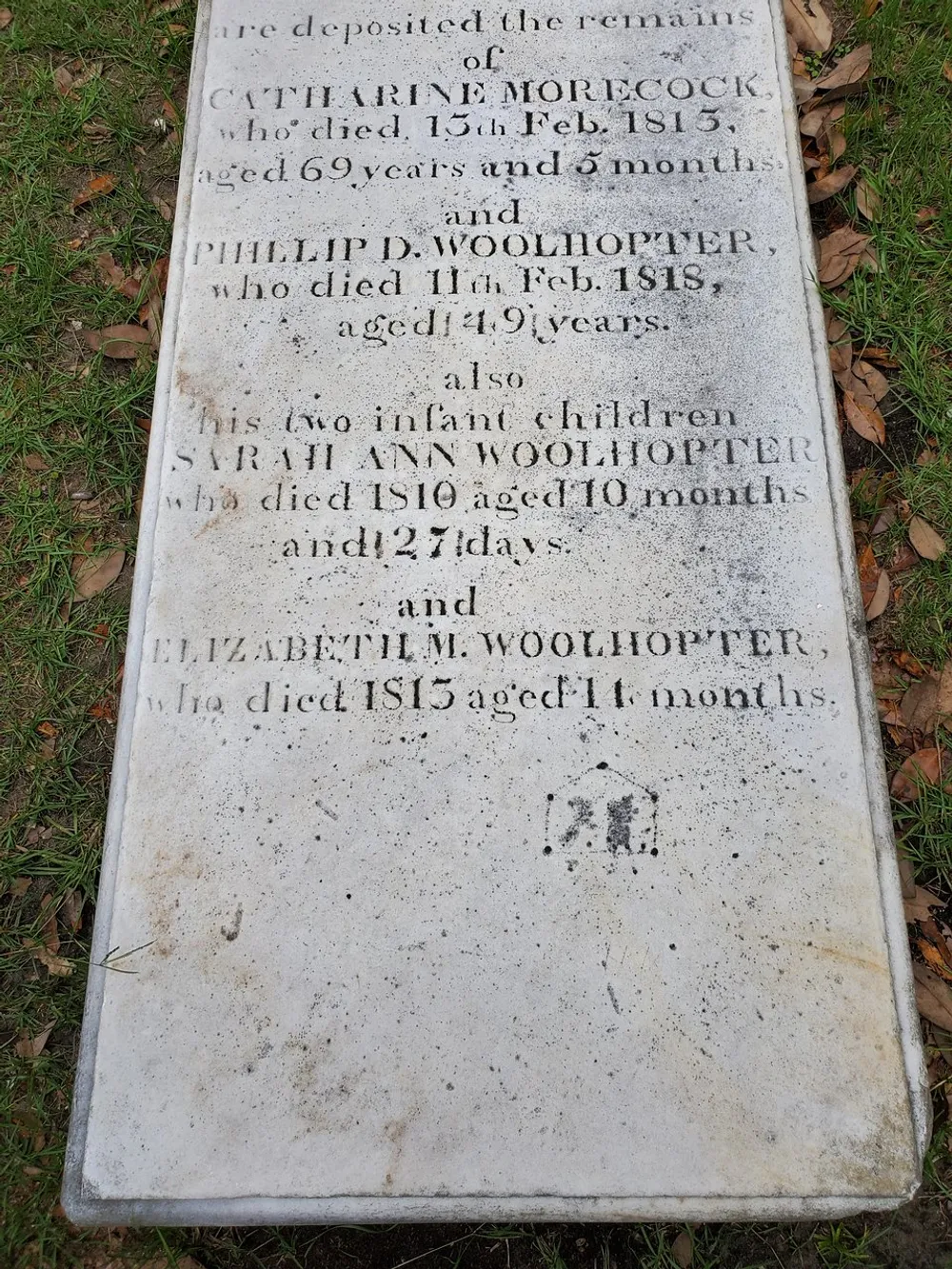The image shows an old gravestone lying flat on the ground with inscriptions marking the resting places of Catharine Morecock Philip D Woolhopter and their two infant children dating back to the early 19th century