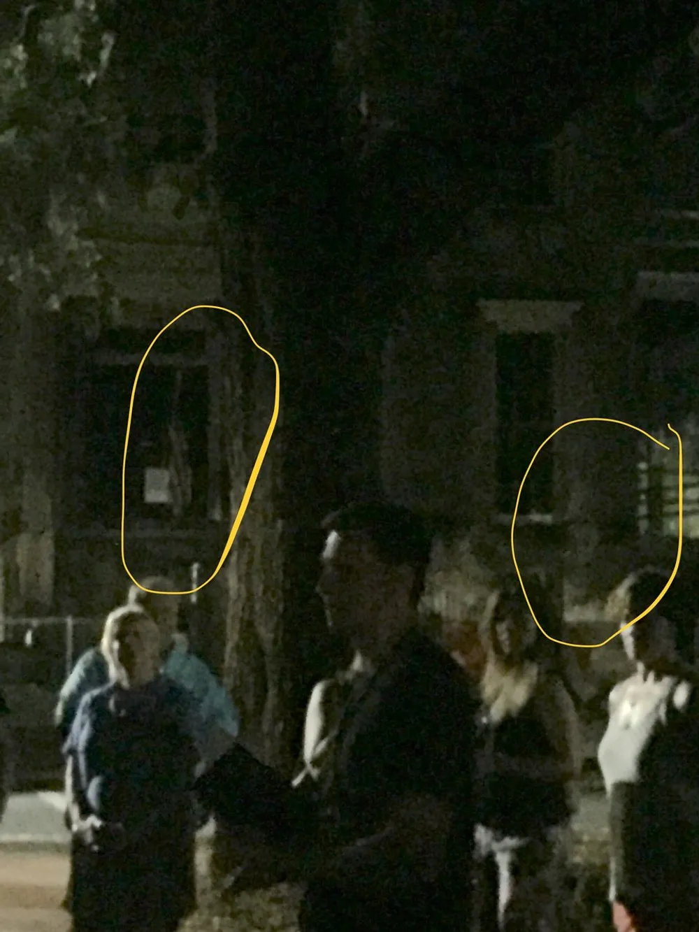 The image shows a group of people gathered at night with two areas highlighted by yellow ovals possibly indicating points of interest or anomalies within the scene