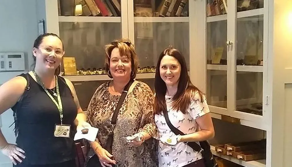 Three women are smiling for the camera indoors possibly during a group event or visit with each holding a small item in their hands