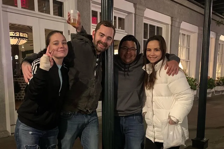 Four people are posing happily for a photo at night on an urban street, with one of them raising a glass in a toasting gesture.