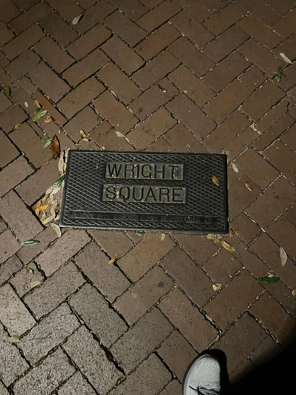 The image shows a plaque on a brick pavement reading WRIGHT SQUARE with some leaves scattered around it and the corner of a persons shoe visible at the bottom