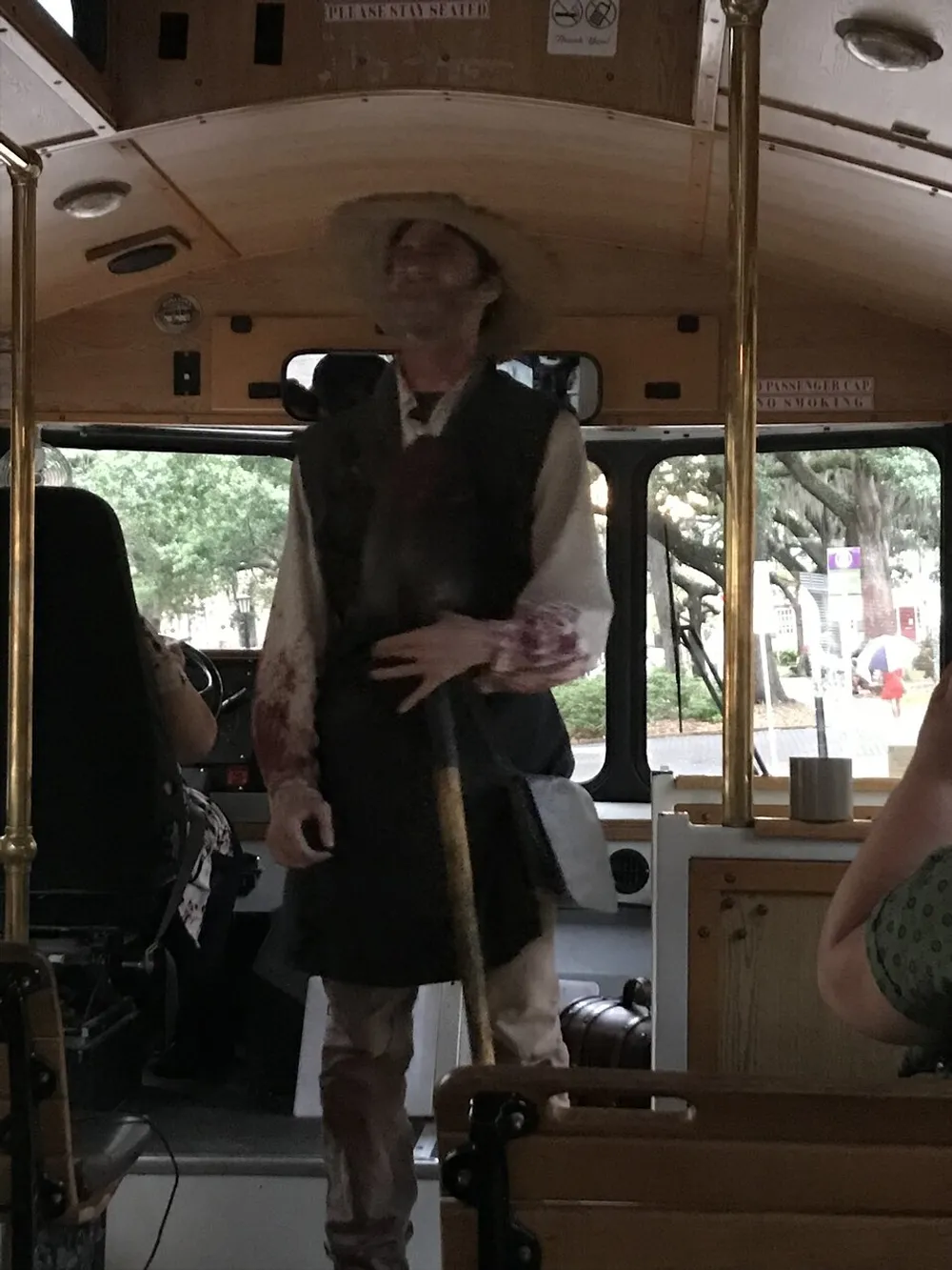 A person in period clothing potentially a tour guide is standing in the aisle of a trolley bus addressing the passengers