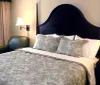 The image shows a neatly made bed with a floral patterned comforter flanked by matching nightstands with lamps against an elegant black headboard in a well-lit room with fresh flowers adding a pop of color