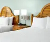 This image shows a neatly made bedroom with two twin beds featuring unique curved wooden headboards white bedding and a shared nightstand with a lamp and a clock