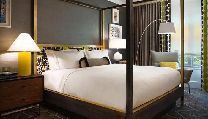 This image shows a modern bedroom with a stylish four-poster bed contemporary lamps and accents of yellow and black creating a comfortable and chic space