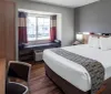 The image shows a tidy and contemporary hotel room with a large bed a window seat and a flat-screen TV