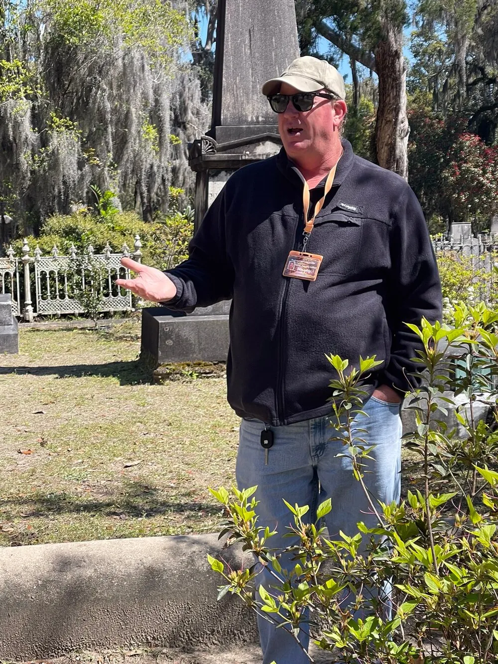 A person is giving a tour or presentation outdoors possibly in a historical or cemetery setting while gesturing with their hand