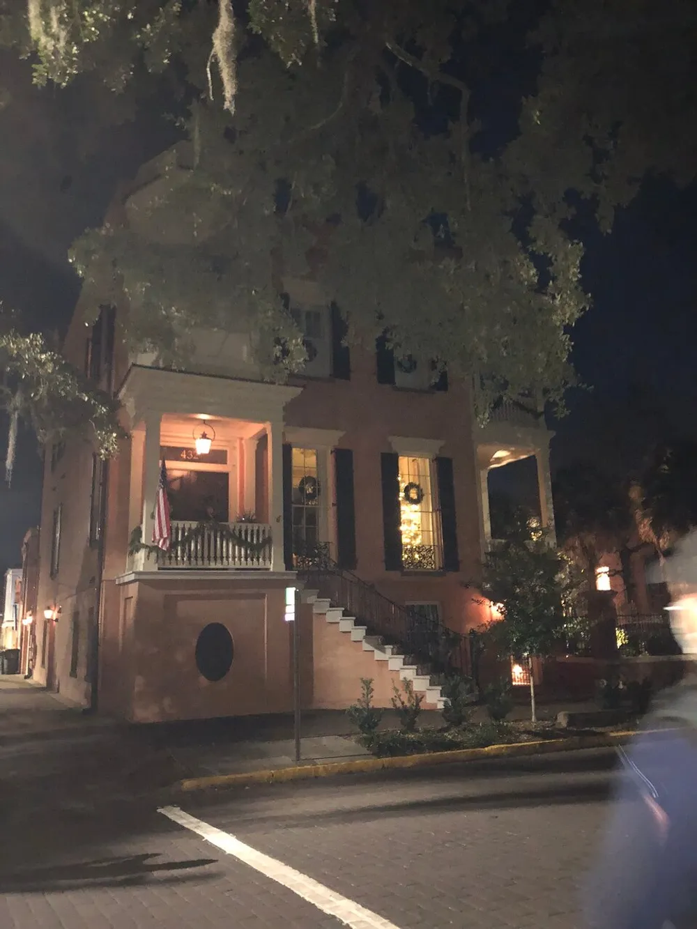 The image shows a stately brick building at night illuminated by exterior lights with a grand staircase leading to an entrance flanked by large windows and draped with Spanish moss-laden trees overhead